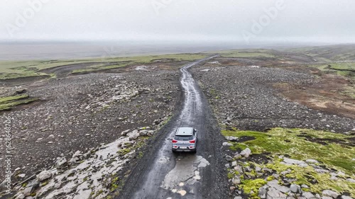 Silver SUV embarking on an Icelandic adventure on a gravel road full of potholes on a rainy day