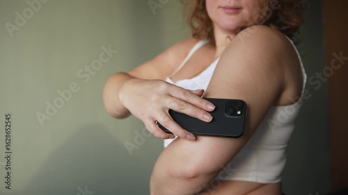 Young woman controls blood sugar level using sensor and smartphone. Continuous glucose monitor helps diabetic to independently control condition and amount of sugar in blood at home.