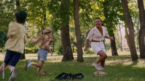 Multiethnic group of energetic children running around in park playing tag while having fun after school classes on green lawn celebrating beginning of summer vacation