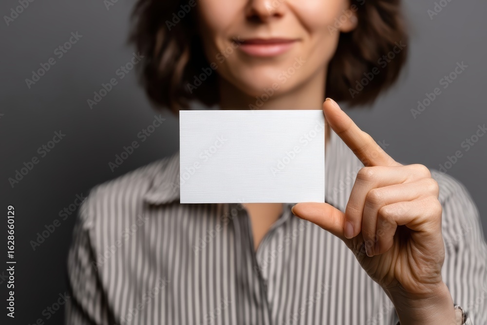 A woman in a striped shirt holds a blank white business card in front of her, ready for customization or branding A woman in a striped shirt holds a blank white business card in front of her, ready for customization or branding