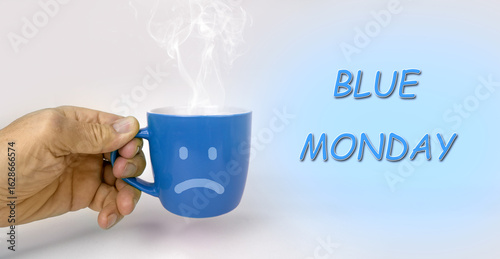 Male hand holding blue cup. Blue Monday concept. Sad face drawn