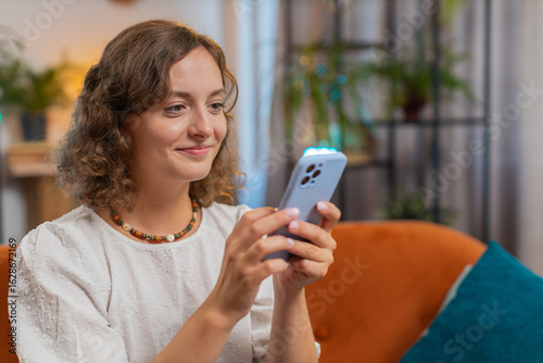 Papier peint Portrait of young woman sitting on sofa using mobile phone smiling at home living room apartment