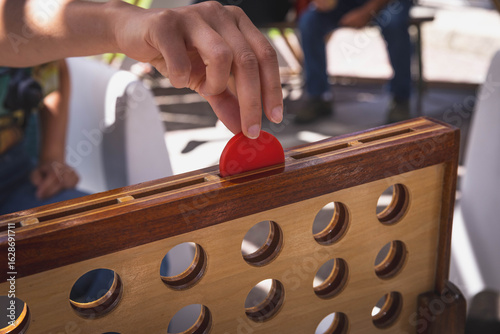 Dropping a red token in a wooden Connect Four game outdoors