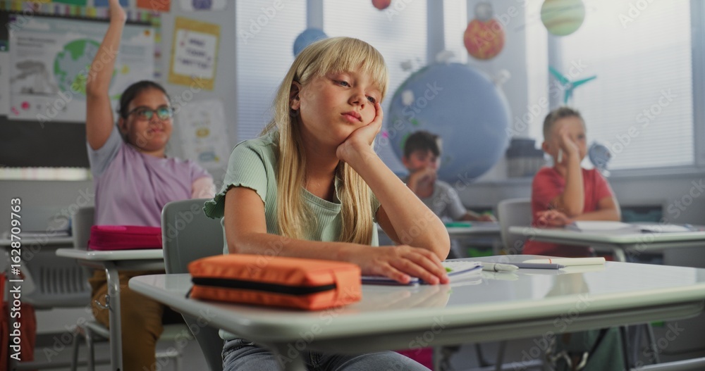 Fototapeta premium Sad Primary School Girl Sitting at Desk, Getting Tired During Lesson or Upset Because of Bad Grade on Homework. Group of Young Children Learning Science or Geography in Modern Classroom. Dolly Shot.