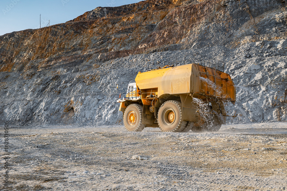 Obraz premium Anti-dust watering Dump Truck in Open-Pit Mine Against Rocky Terrain.