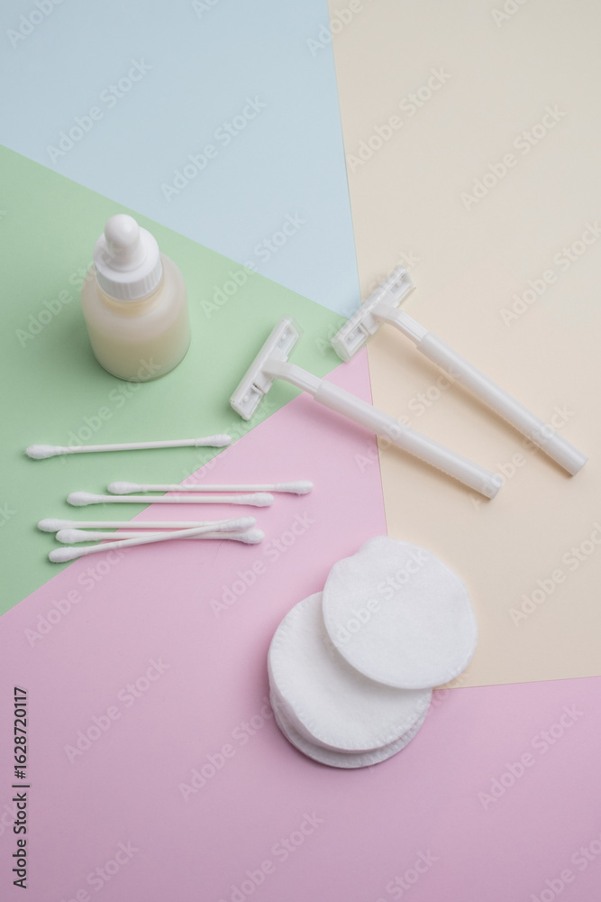 Fototapeta premium White razor with cotton pads and sticks, face cream or serum on pastel background. Self-hygiene, beauty concept.