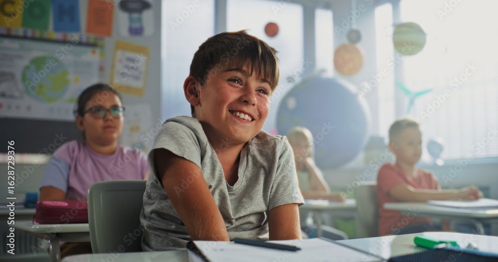 Obraz premium Primary School Boy Sitting at Desk, Raising Hand and Giving Correct Answer on Teacher's Question During Geography Lesson. Group of Young Boys and Girls Learning Science in Modern Colorful Classroom.