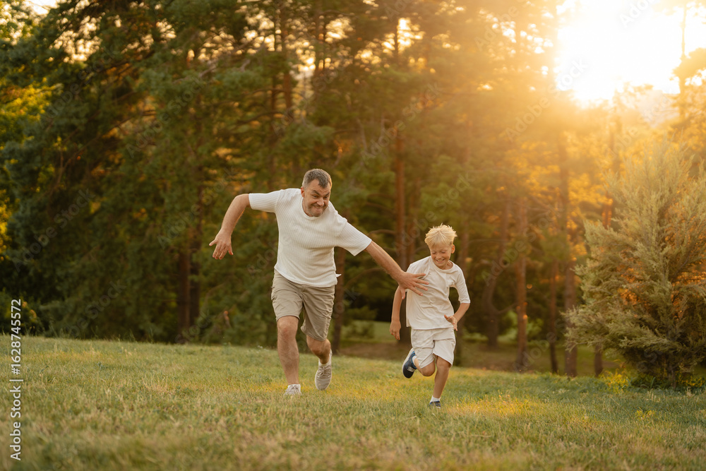 Fototapeta premium Father and son playing and running together outdoors during a sunny evening