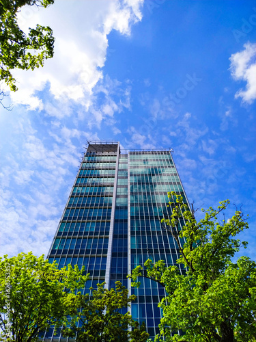 Modern Glass Skyscraper and Green Trees Against Blue Sky