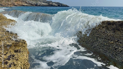 Small waves gently splash through natural stone slabs on Kory Beach in Alanya, Turkey. Peaceful seaside view perfect for travel, relaxation, and nature themes