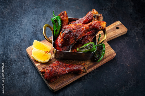 Authentical barbecue hot spicy chicken tandoori curry masala drumsticks with grilled chillis and lemon served as closeup in a bowl