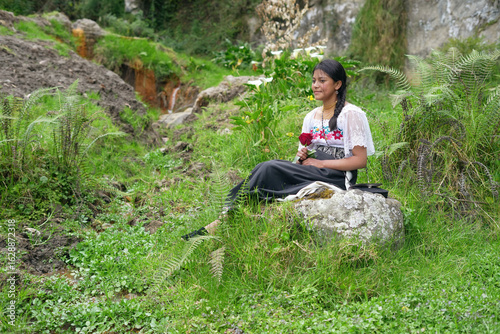 Indigenous otavalo girl sitting on rock holding red rose in ecuadorian andes mountains