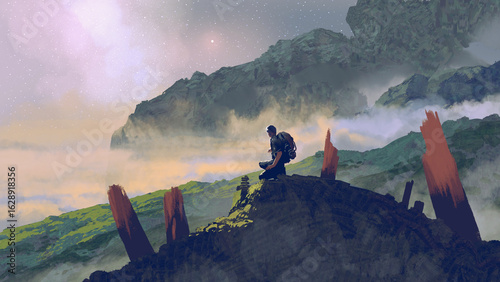Fotografie A lone traveler kneels on a rocky mountain peak surrounded by misty valleys bene