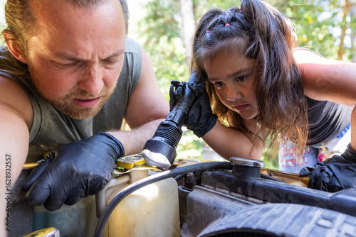 A man looks under the hood of a car while a young girl holds the flashlight, and passing down practical skills., helping him with the repair. Heartwarming outdoor scene illustrating family bonding, te