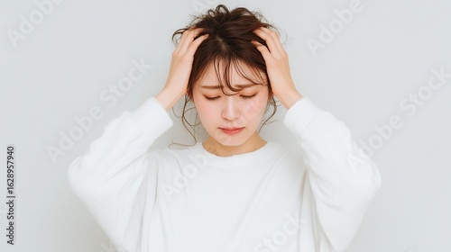 頭を抱えて思い悩む女性　白背景でストレスや不安を表現