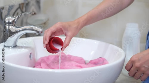 A person preparing to wash pink clothes in a sink. Using white detergent or washing powder, demonstrating a home laundry routine.