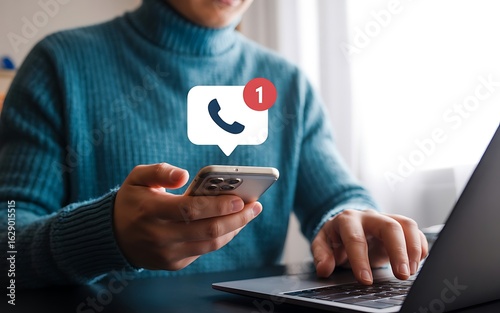 Businesswoman using a smartphone with a missed phone call notification while working on a laptop. Modern technology and communication concept.