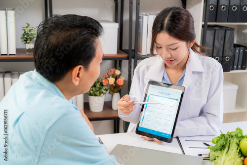 Asian nutritionist using tablet to explaining personalized meal plan with AI to patient during healthcare consultation, healthy lifestyle, woman dietitian showing nutrition plan with AI on tablet.