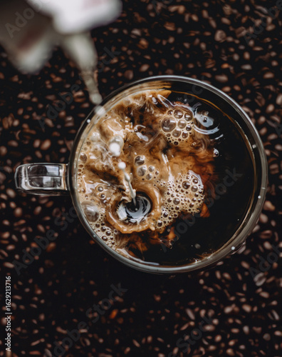 Cream Swirling in Fresh Black Coffee with Coffee Beans Background - Top View