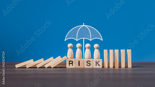 A business team at the workplace is protected under an umbrella while falling dominoes are stopped, illustrating risk management, insurance protection, and safety strategy in organizations