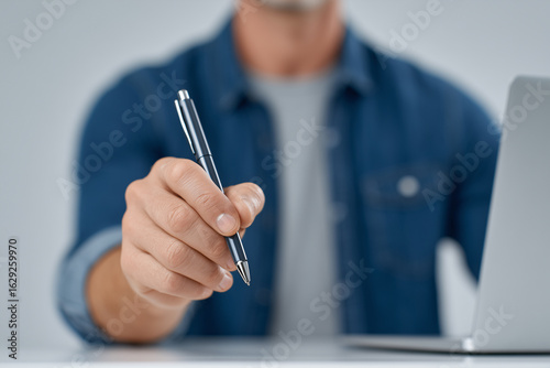 Pen in Hand: A focused individual presents a sleek pen, ready to sign or write, symbolizing ideas, agreements, and commitments in a professional setting.