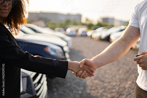 Photography A female car dealer shakes hands with a man after a car purchase, sealing the deal in a dealership