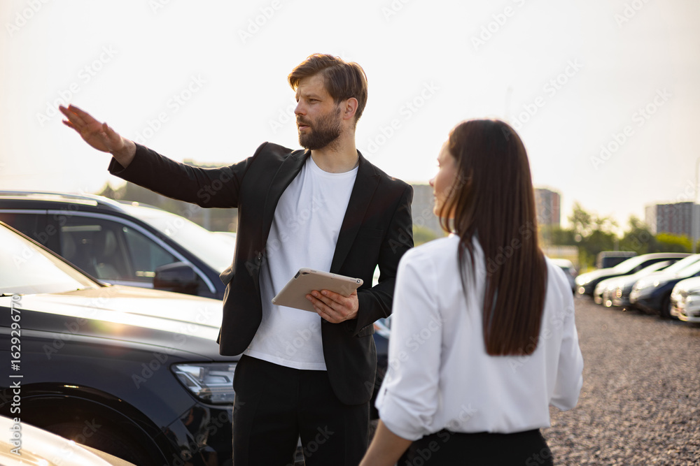 Obraz premium A male car dealer explains a vehicle to a woman at a car dealership.