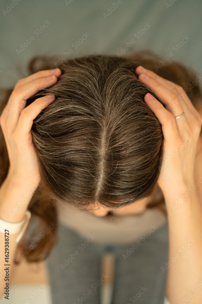 Fototapeta premium Close-up view from above of a woman touching her scalp and showing gray roots. Beauty in aging, self-acceptance, and gentle hair care. Natural transformation, soft light, healthy texture.