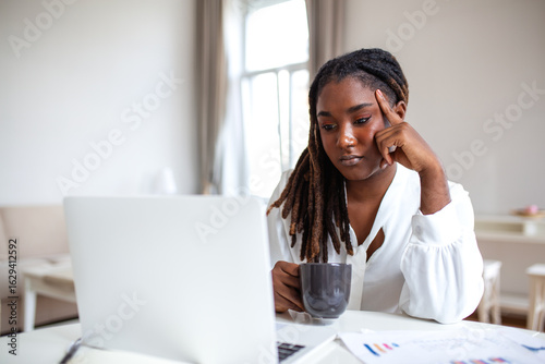 Photography Serious frowning African American ethnicity woman sit at workplace desk looks at laptop screen read e-mail feels concerned
