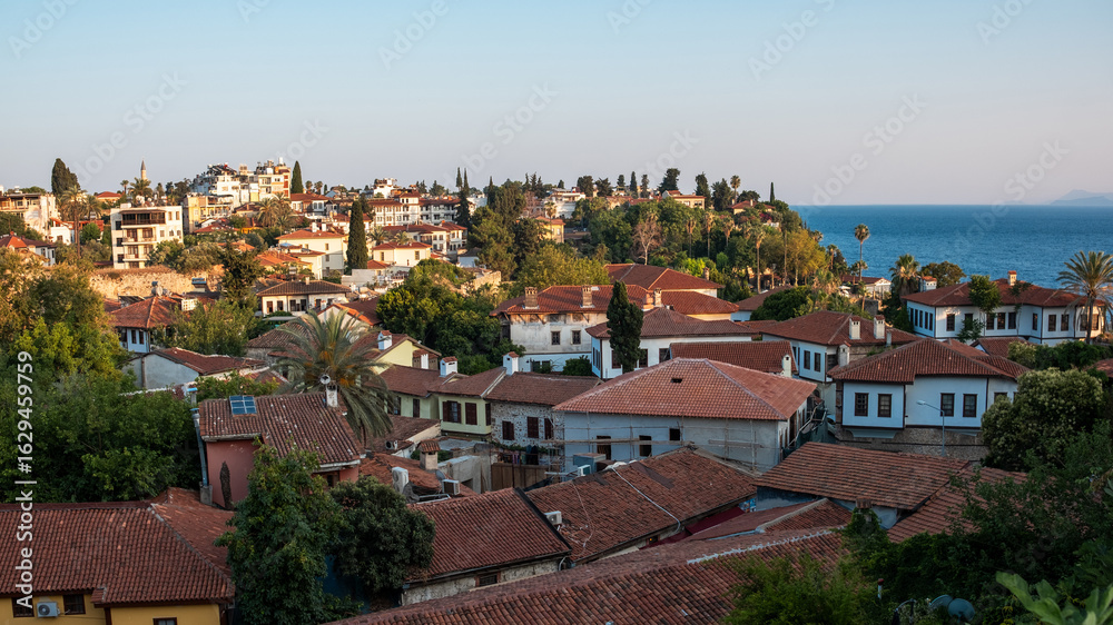 Obraz premium Quaint villages with red-tiled roofs and lush greenery overlook the calm Mediterranean Sea in the warm glow of evening light.