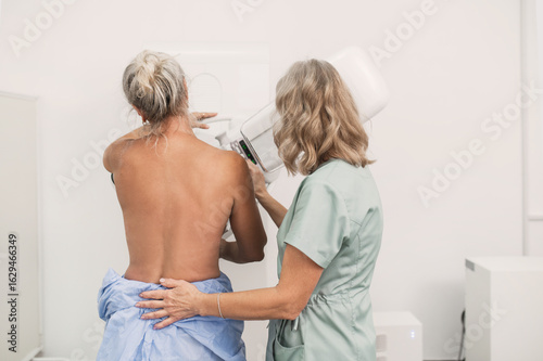 Billede på lærred 50-year-old woman undergoes mammography procedure on special medical equipment mammograph with the help of assistant in modern clinic