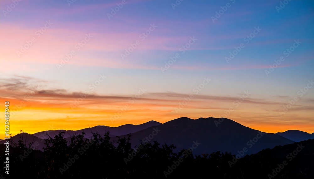 Obraz premium Mountain range silhouette under a vibrant sunset sky with orange and purple hues