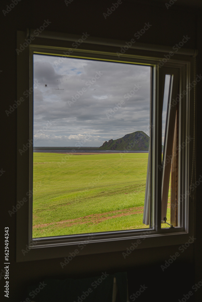Fototapeta premium View Through a Window of Green Field, Rocky Hill, and Coastline