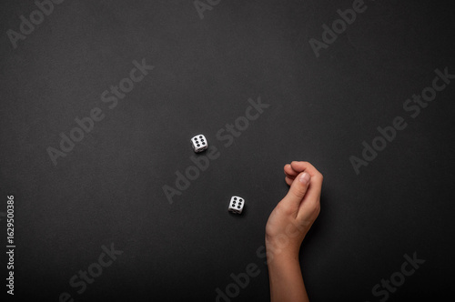 Child's hand rolling dice on a black background. 