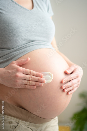 Glowing mother-to-be massaging cream onto her rounded abdomen. Nourishing skincare moment for maintaining healthy skin during gestation.