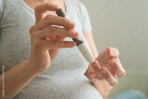 Close-up of pregnant female using glucometer to measure blood sugar levels. Vital health check for preventing gestational diabetes complications.