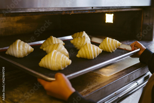 Baker putting a tray of uncooked croissants into oven.