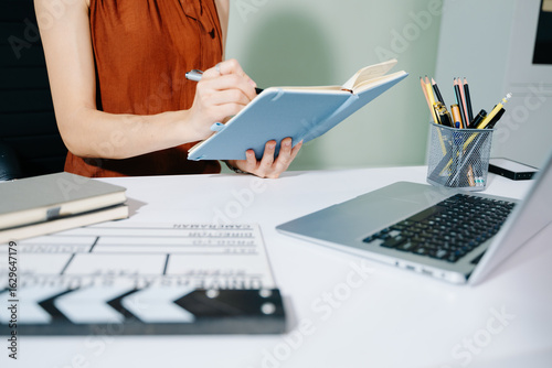 Creative female filmmaker working with tablet, clapperboard, and laptop in modern studio office. Film production, planning, and content creation scene.
