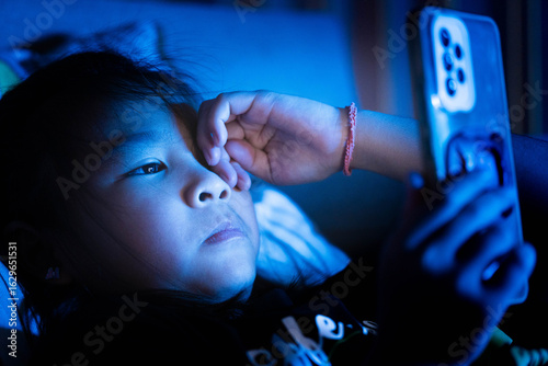 Bilde på lerret Little Asian girl using smartphone in bed at night, screen light on face