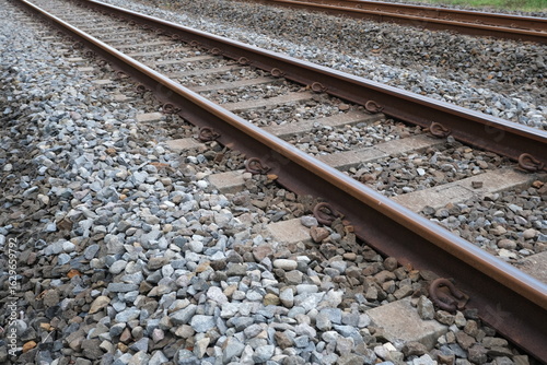 Obraz na plátně Detailed view of parallel railway tracks with metal rails and wooden sleepers surrounded by crushed stone ballast for support