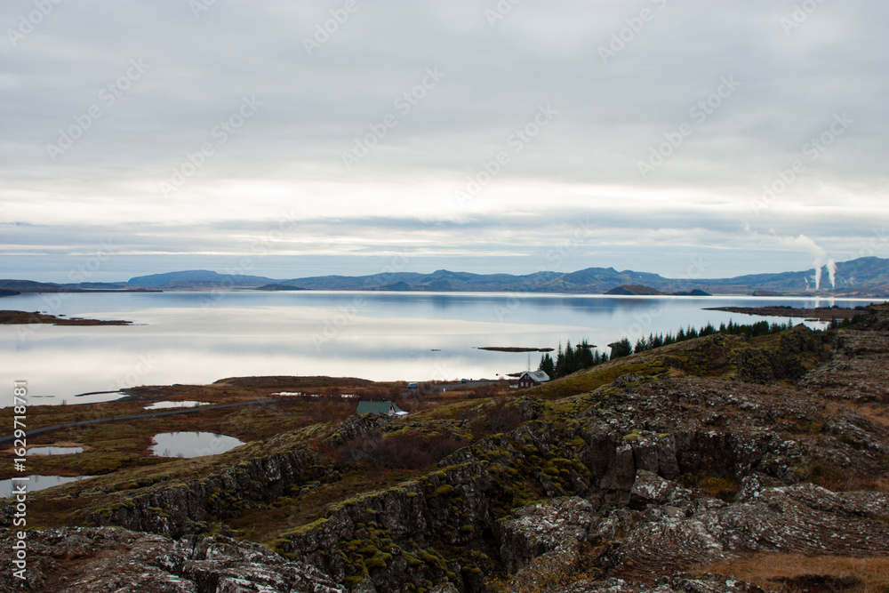 Naklejka premium Autumn mountain landscape with a scenic lake reflecting the forest and cloudy sky in Nordic landscape, Iceland