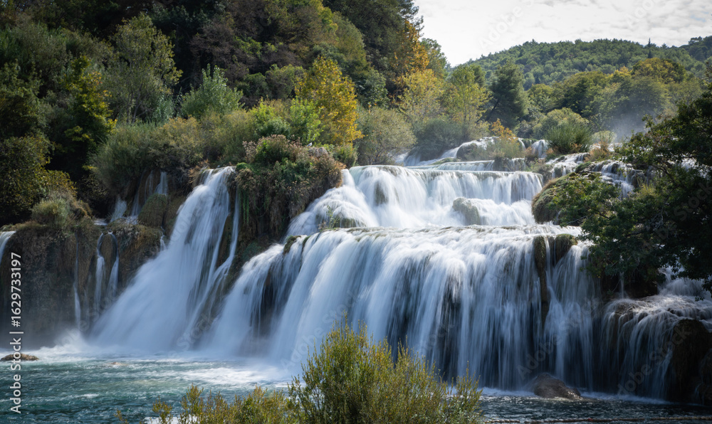 Fototapeta premium Peaceful waterfall in a Croatian national park surrounded by lush greenery and clear water. A stunning natural landscape ideal for travel, nature, adventure, and outdoor-themed content