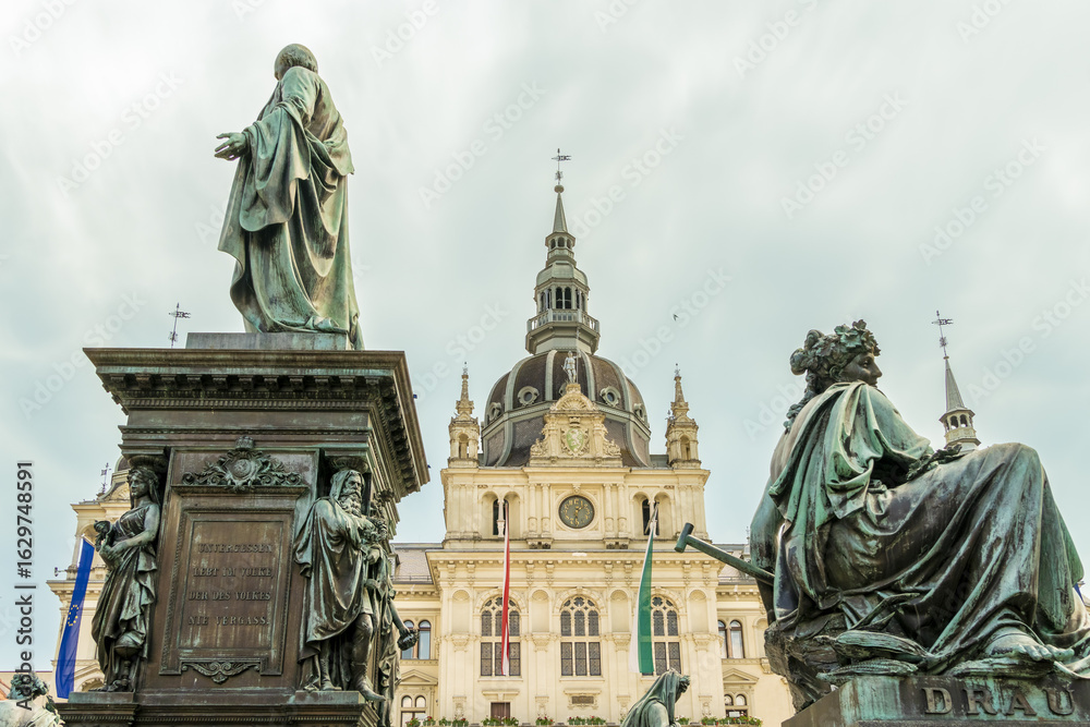 View of the Archduke Johann Fountain, a majestic bronze sculpture with classical figures, contrasting against the ornate Graz City Hall, Graz, Graz, Austria. View of the Archduke Johann Fountain, a majestic bronze sculpture with classical figures, contrasting against the ornate Graz City Hall, Graz, Graz, Austria.