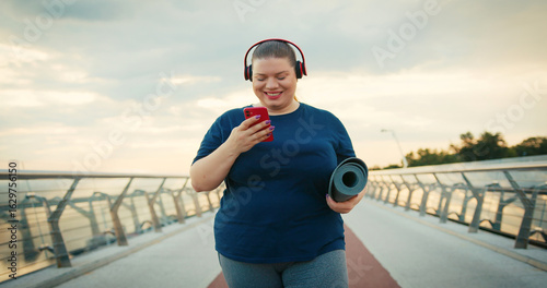 Outdoor Portrait of Body Positive Overweight Woman Using Red Smartphone Phone Outdoors at City in the Morning. With Red Headphones