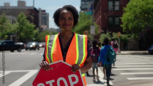 Friendly african american crossing guard protecting schoolchildren while stopping traffic, helping students cross street safely near urban school building