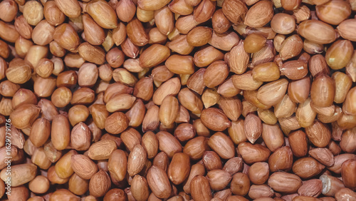 A close-up view of numerous unpeeled peanuts, filling the frame completely.  The peanuts are reddish-brown and appear dry.