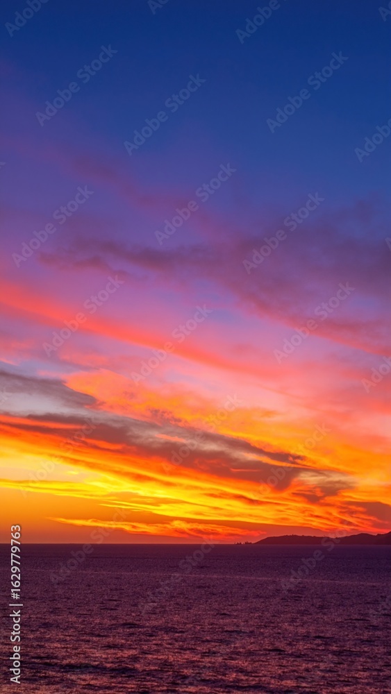 Fototapeta premium A vibrant sunset paints the sky in hues of orange, pink, and purple, reflecting beautifully on the calm ocean waves, creating a serene coastal scene.