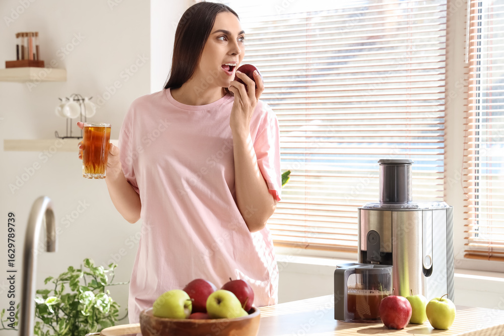 Young woman with modern juicer eating apple in kitchen Young woman with modern juicer eating apple in kitchen