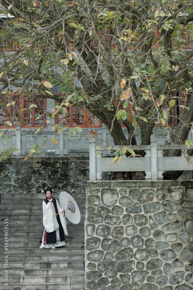 Obraz premium Young Asian female in traditional attire with parasol outdoors.