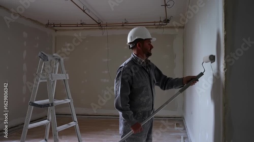 Skilled painter rolling white paint on unfinished wall interior, stepladder standing nearby during home renovation process